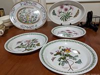 Three round collectible plates and one oval baking dish arranged on table, showing botanical and floral designs