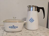 Both the blue cornflower coffee percolator and covered casserole dish shown together on a table.