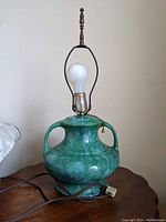 Front view of green glazed ceramic lamp showing bulb and socket with pull chain, placed on wooden surface.