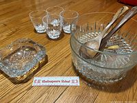 Photo showing two large cut glass salad bowls, wooden teak salad servers inside one bowl, four small cut glass rock glasses, and a large cut glass ashtray.