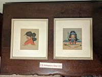 Two framed mid century art prints placed side by side on a table, showing full frames and visible matting. A ruler is placed below for scale.