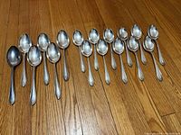 Full set of 17 silver plated spoons (6 serving spoons and 11 tablespoons) laid out on wood floor.