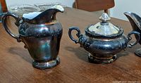 Silvered porcelain creamer and sugar bowl side by side, showing the creamer's broken spout.