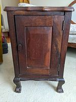 Front view of the small antique wooden cabinet showing the paneled door and claw feet.