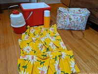 Image showing a yellow floral vinyl hanging organizer laid out, vintage floral insulated cooler bag, yellow-orange Thermos vessel, large red and white cooler jug, and red cooler without lid on a carpet.