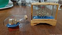 Photo showing both miniature ship in bottle and tiny ship model in glass case, with six-inch ruler for scale visible in background.