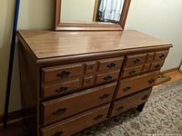 Front view of vintage wooden dresser showing multiple drawers and ornate metal handles with a large wooden mirror leaning against the wall behind it.