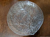 Top-down photo of the round, textured glass canape plate showing the detailed fir branch Furu pattern.