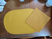 One oval mustard yellow woven placemat with one matching napkin folded and placed on top, showing texture and color.