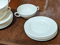 Cream-colored Wedgwood Edme pattern small two-handled bowls and stacked plates showing ribbed edge detail on plates and cups.