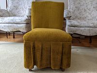 Front view of the vintage skirted slipper chair showing the green-gold textured upholstery and box-pleated skirt.