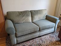 Full front view of green velour microfiber sofa with two seat cushions and two back cushions, positioned against wall, placed on patterned area rug.