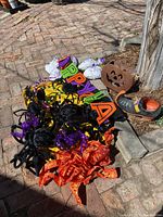 Photo of multiple Halloween decorations on patio including large and medium glitter spiders, metal pumpkin decoration, glitter shoe, and Halloween banner laid out on the ground.