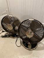 Two heavy, retro style Hunter brand metal table fans placed on the floor, showing front and side views.