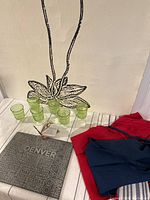 Overview photo showing 6 green glasses or candle holders, 1 slate cheese board with Denver and Colorado city names, and 2 linen aprons in red and navy blue.