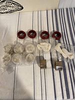 All 12 napkin rings arranged on striped cloth; 4 burgundy plastic rings and 8 silver metal rings in plastic bags