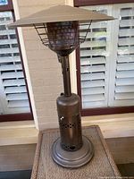 Full view of propane patio table heater showing top reflector, protective cage, central post and round base.