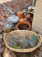 Wide view of assorted pots, vases, basket, and garden decorative items arranged on brick patio.