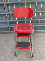 Front view of red metal vintage chair with fold-out steps showing red seat and backrest, chrome frame, and two black rubber steps.