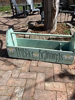 Front view of the painted wooden tool box showing 'Embrace Beginnings' inscription with flowers