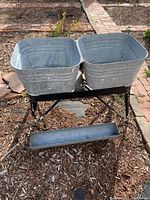 Wide shot of vintage double washstand with two square galvanized basemetal buckets on metal frame outdoors on mulch.