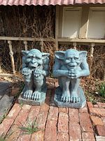 Two poly fiber gargoyle statues in crouching pose with hands resting on knees, faux stone finish, grayish-blue, displayed outdoors on brick pavers
