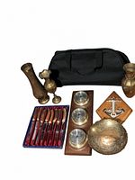 Photo of brass vases, black bag, brass bowl, wooden plaque with instruments, and steel cutlery set in a blue and red box.