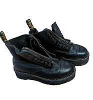 Side angle view of the black leather platform boots showing the pebbled texture, front zipper partially unzipped and yellow stitching around sole.