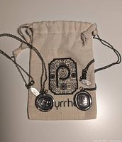 Two Pyrrha necklaces on branded drawstring pouch showing both pendants and chains