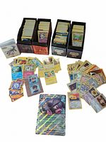 Three cardboard Pokemon TCG deck boxes filled with assorted cards, spread cards in front, jumbo card at bottom