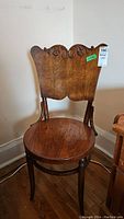 Front view of antique wooden arts and crafts chair showing carved backrest and circular nail-patterned seat.