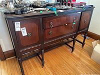 Front and side view of an antique wooden sideboard with two drawers and two cupboards. Shows inlaid wood details and brass hardware.