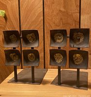 Front view of both brutalist metal bookends showing four concave square plates with central textured circles per bookend.