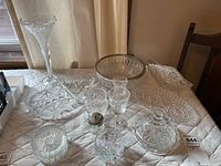 Wide view of the entire lot showing various crystal and pressed glass bowls, trays, glasses and a tall vase arranged on a quilted surface