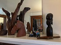 View of entire collection on a mantel featuring driftwood sculpture, stone horse head, ebony figure, painted elephants, and ceremonial cutter