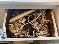 Photo of wooden drawer filled with various indoor extension cords, mostly beige and brown in color, tangled with plugs and surge protectors.