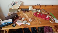 Full lot arrangement on wooden table showing assortment of eyeglasses, jewelry, brooches, fan, mirror, pouch, and tray