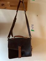 Full view of the front of the leather satchel hanging, showing strap and handle
