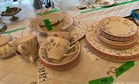 Wide view of multiple Johnson Brothers china items including stacked teacups with saucers, plates, and serving bowls with floral pattern and red trim showing overall condition and design.