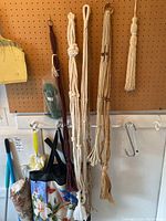 Photo showing macrame plant hangers and metal hooks hanging on pegboard with other cleaning tools.