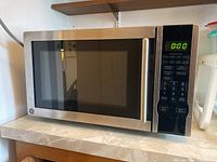 Front view of the microwave showing stainless steel body, black glass door, and handle.
