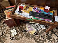 Top view of music books, small red kazoo, pitch instrument, metronome, and black zipper pouch inside bench lid.