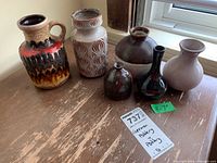 All six ceramic pottery items arranged by a window with varied shapes and glazes