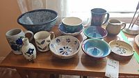 Photo showing 11 various artisan pottery items including bowls, a mug, small vases, and dishes with floral and abstract designs.