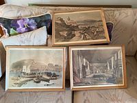 Three framed antique reproduction prints showing different Quebec scenes on a couch including cityscape with cannons, harbor with ships, and interior room.