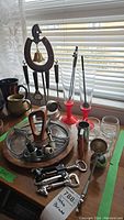 Wide view of entire barware lot on a table in front of window showing drink caddy, glasses, sectioned server, and corkscrews.