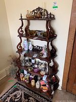 Full view of vintage five-tier wooden display shelf containing various small decorative items. Shelf shows ornate scroll and carved accents and dark wood finish with signs of wear.