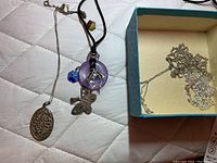 Three necklaces with various pendants including filigree oval, amethyst with dolphin, butterfly and blue enamel clover, all on a quilted fabric.