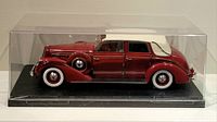 Side view of the diecast red vintage car model inside a clear display case on a black base.