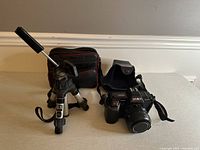 Minolta camera, soft case, and compact tripod arranged side by side on floor.